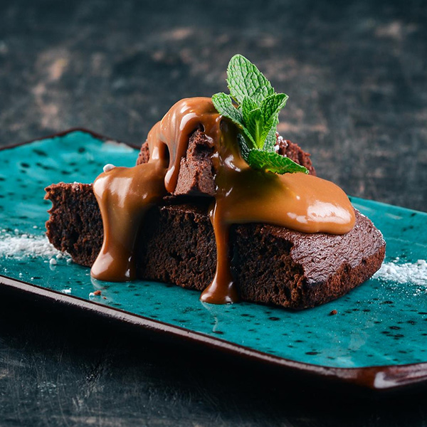  fudge brownie served on a plate with vanilla icecream with almond brownie bits and caramel sauce